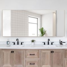 a bathroom vanity with two sinks and a large mirror above it, in front of a potted plant