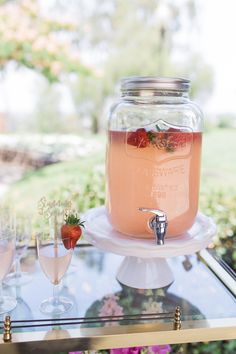 a table topped with glasses filled with liquid and strawberries next to a jar full of water