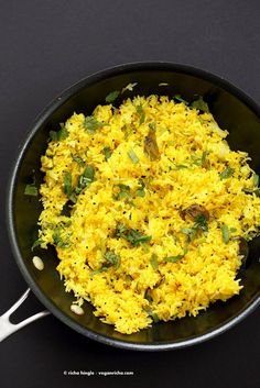 a pan filled with yellow rice on top of a black table next to utensils