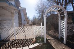 an outdoor area with a white trellis and stone steps leading up to the house