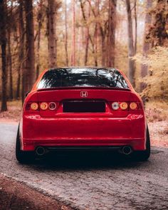 the back end of a red car parked on a road in front of some trees