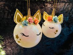 two glass ornaments with unicorn faces and flowers on them hanging from a christmas tree branch