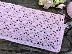 a pink crocheted blanket next to some yarn and flowers on a wooden table