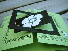 three green cards with white flowers on them sitting on top of each other in front of a wooden bench