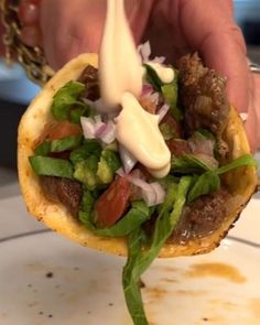 a hand holding a sandwich with meat, lettuce and tomato on it while being drizzled with mayonnaise