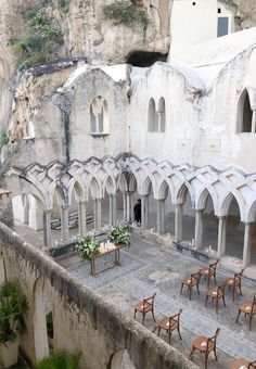 an old building with tables and chairs in the courtyard next to a cliff side area