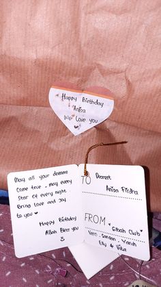 two birthday cards are on top of a bed with pink sheets and pillows in the background