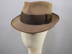 Get your Sam Spade look in an instant with this vintage 40s fedora. The light brown felt body is accented with a chocolate brown ribbon band and flat bow. It has a deep teardrop bash at the top, with a pinch at the sides that comes to a sharp point at the front.  Its slightly distressed look could also be described as broken in, or "having the patina of age"...however you say it, it's not perfect, which is how the hat of any rakish private detective should be. The wide brim has the chocolate brown ribbon at the edge, which serves to highlight a few uneven waves and the tipped angle it seems intent on keeping, at least without professional intervention of high steam and blocking. The back of the teardrop bash is lower than the front, which seems appropriate in a hat with so much going on. T Mens Hats Vintage, Brown Ribbon, Private Detective, Vintage 40s, Men's Hats, Bow Flats, Hat Band, Fedora Hat, Wide Brimmed