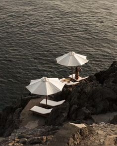 three umbrellas are set up on the edge of a cliff by the ocean with people sitting under them