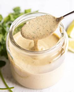 a spoon full of mayonnaise sitting on top of a jar filled with sauce