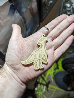 a person's hand holding a wooden dinosaur keychain