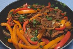 a pan filled with meat and peppers on top of a blue table cloth next to a fork