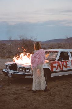 a woman standing in front of a car with flames coming out of the back door