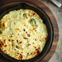 a skillet filled with cheese and broccoli on top of a wooden table