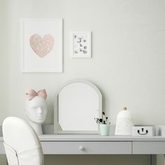 a white desk topped with a chair next to a mirror and pictures on the wall