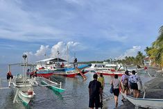 several boats docked in the water with people walking around them