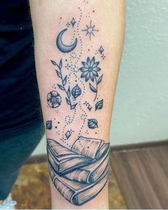 a tattoo on the arm of a woman with an open book, stars and moon