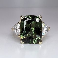 a fancy green diamond ring with three diamonds on the sides and an emerald colored stone in the middle