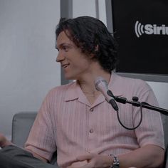 a man sitting in front of a microphone talking into a microphone with another person standing next to him