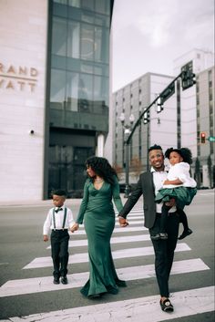 a man and woman walking across a cross walk holding hands with a child in their arms