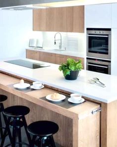 a modern kitchen with white counter tops and wooden cabinets, along with black bar stools