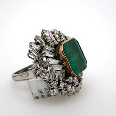 Vintage emerald with diamonds ring, circa 1970's.  Approximately 13.00ct emerald apx F2 surrounded by apx 5.30ct of round and baguette diamonds. Apx 18.30ct total gemstone weight, set in 18k white gold. Accommodated with an up-to-date digital appraisal by a GIA G.G. once purchased, upon request. Please contact us with any questions.  Emerald Cut Emerald = Approximately 13.00ct  Round and Baguette Cut Diamonds = Approximately 5.30ct, G/H color and VS/SI clarity  Total Gemstone Weight = Approximately 18.30ct 18-Karat White Gold Size 6.25, can be sized upon request Emerald Ring With Baguette Diamonds Gift, Emerald Ring With Baguette Diamonds In Fine Jewelry Style, Emerald Ring With Baguette Diamonds Fine Jewelry, Formal Green Diamond Ring With Baguette Diamonds, Elegant Emerald Ring With Baguette Diamonds For Formal Occasions, Green Diamond Rings With Baguette Cut, Green Baguette Diamond Rings, Luxury Green Rings With Baguette Diamonds, Luxury Green Emerald Ring With Baguette Diamonds