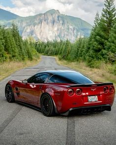 a red sports car parked on the side of a road in front of a mountain