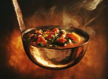 a metal bowl filled with food on top of a wooden table and steam rising from it