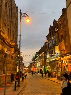 people are walking down the street in an old european city at night with lights on