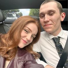 a man and woman sitting in the back seat of a car, smiling at the camera