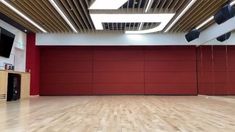 an empty gym with hard wood floors and red partitions on the wall behind it