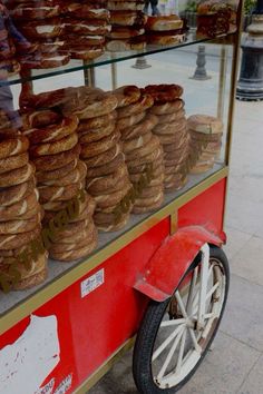 there are many donuts on display in the store window and behind it is a red cart with white wheels