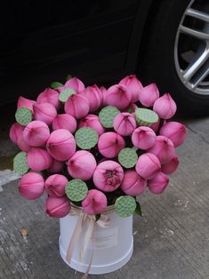 a bouquet of pink flowers sitting in a white vase on the sidewalk next to a car