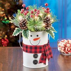 a snowman planter with pine cones and holly in it on a table next to candy