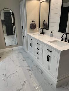 a large bathroom with marble floors and white cabinetry, along with two mirrors on the wall