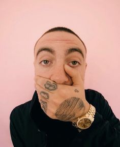 a man covering his mouth with both hands and looking at the camera while standing against a pink wall