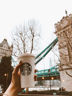 a person holding up a starbucks cup in front of a bridge