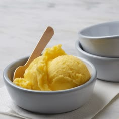 two bowls filled with yellow ice cream on top of a white table cloth and wooden spoons