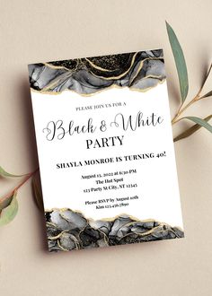 an elegant black and white party card with gold foil accents on the edges is displayed next to some greenery