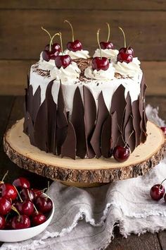 a cake with chocolate and cherries is on a wooden stand next to some cherries