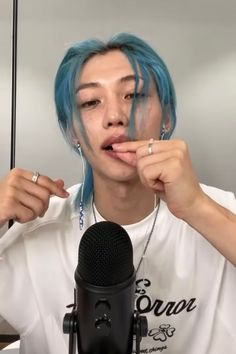 a man with blue hair is holding a microphone and making a silly face while wearing ear rings