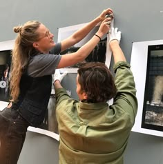 two people are hanging pictures on a wall