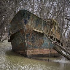 an old rusted boat sitting in the middle of a river with trees around it