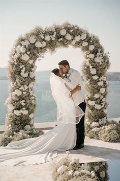 a bride and groom kissing under an arch made of flowers