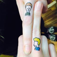 two fingers with small tattoos on them, one has a man's face and the other has a woman's head