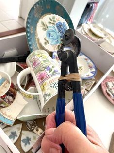 a person holding a pair of scissors in front of some plates and bowls on the counter