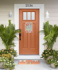 two potted plants sit in front of a red door with a welcome sign on it