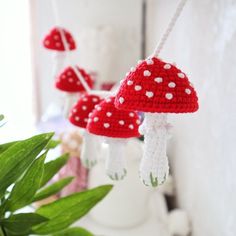 crocheted red mushrooms hanging from strings on a white shelf next to a potted plant