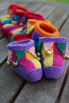 Four pairs of multi-coloured jester booties with jingle bells attached to pointed cuffs sit on a weathered wooden table. Childrens Crochet Hats, Baby Booties Knitting Pattern, Knitted Wit, Knitted Baby, Knitting Ideas, Baby Socks, Baby Sweaters