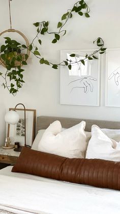 a bed with white sheets, pillows and plants hanging on the wall above it's headboard